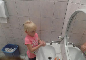Klara ćwiczy prawidłowe mycie rąk przy umywalce.